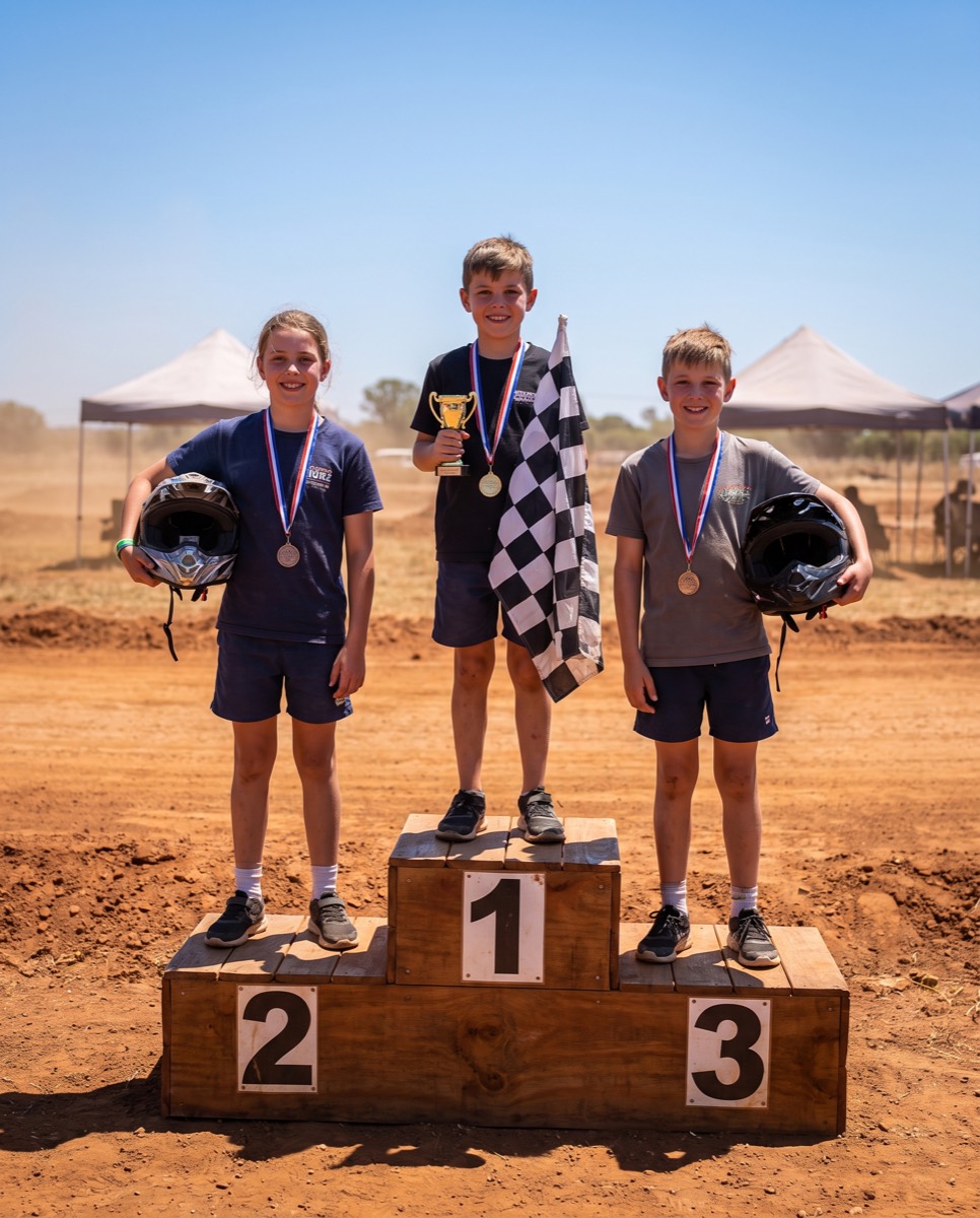 Three kids on a winners podium with medals and a checkered flag